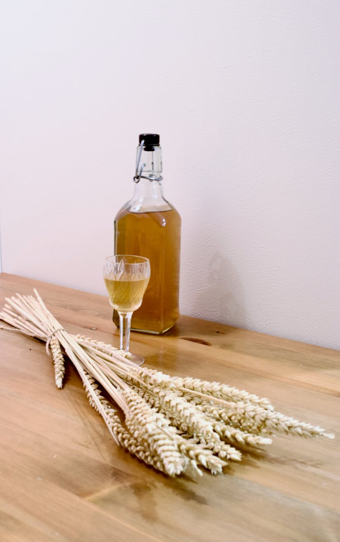 A bottle of wheat whiskey and barley on a wooden surface, evoking a rustic and natural feel.