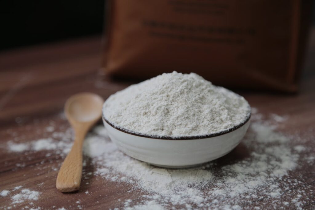 Flour in a ceramic bowl on a wooden surface, perfect for baking and cooking concepts.