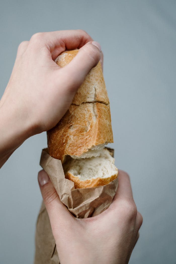 Hands breaking a piece of fresh wheat bread from a bag, evoking a rustic and homemade feel.
