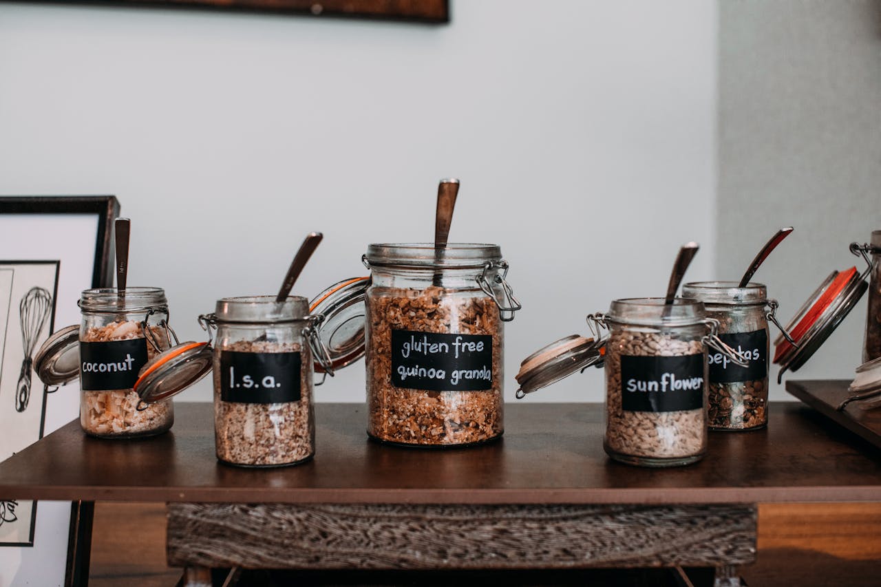 Close-up of labeled glass jars containing various grains and seeds on a wooden table.