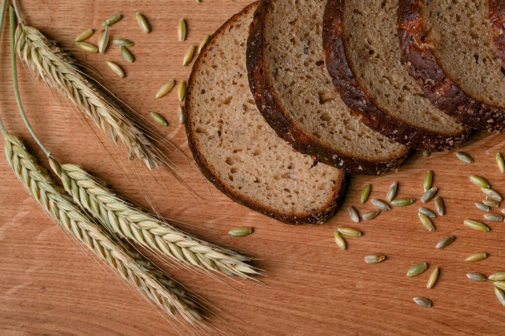 A rustic arrangement of sliced wheat bread with wheat ears and grains on a wooden surface.